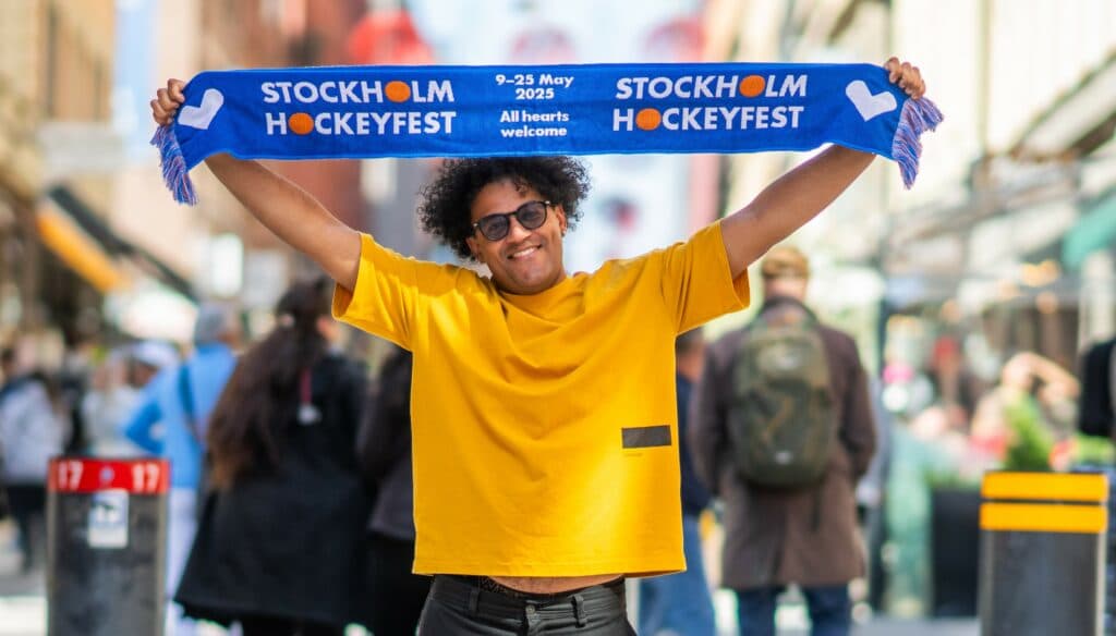 A person holding up a blue Stockholm Hockeyfest scarf on a city street.