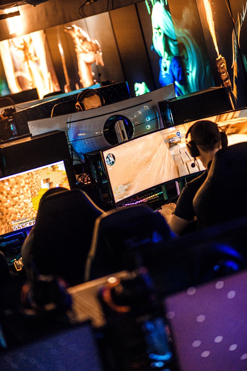 Several people wearing headsets sit at large monitors playing video games in a dark room with colorful lights and game art on the walls.