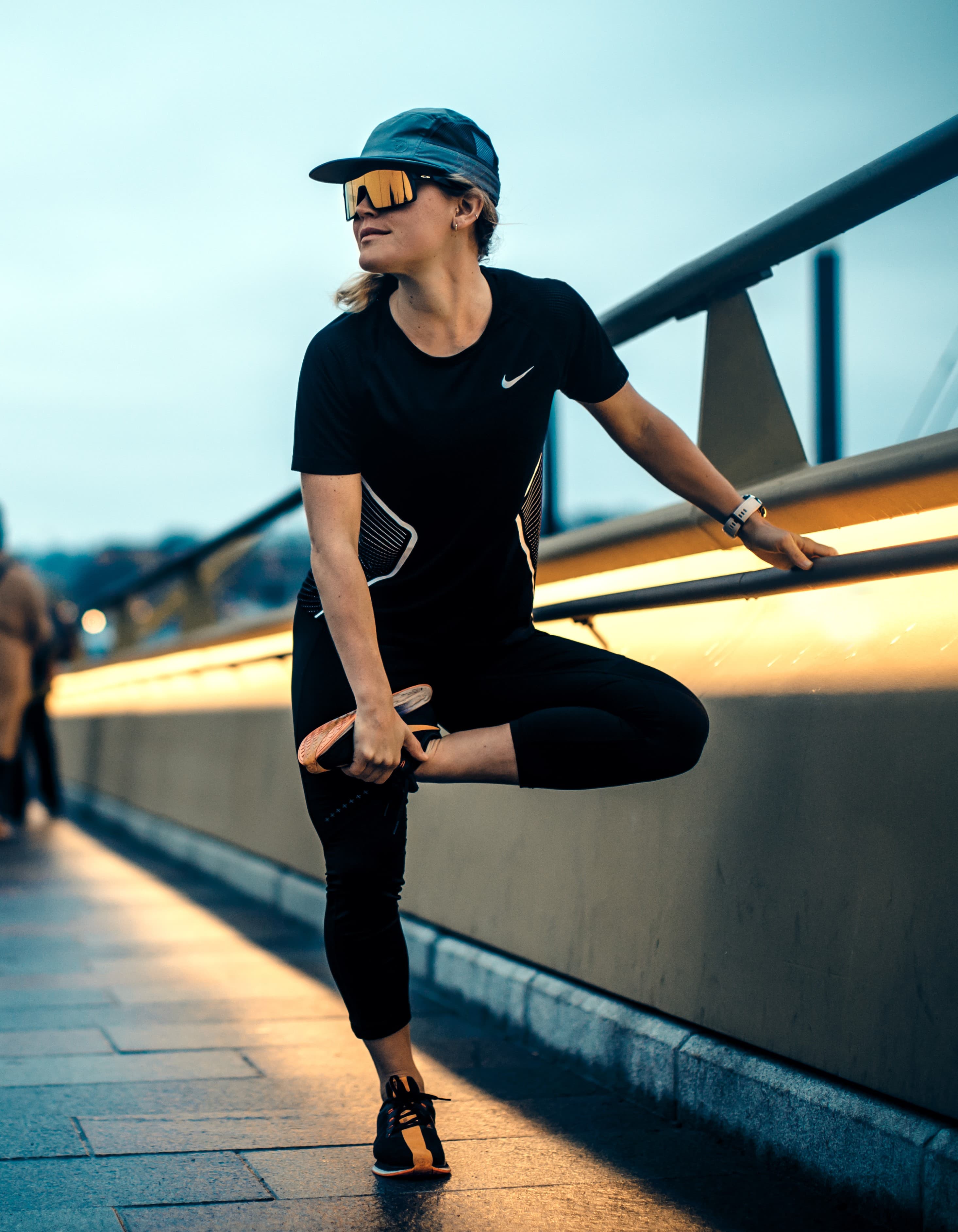 A person in athletic gear stretches their leg on a city bridge, with soft light creating a focused mood.