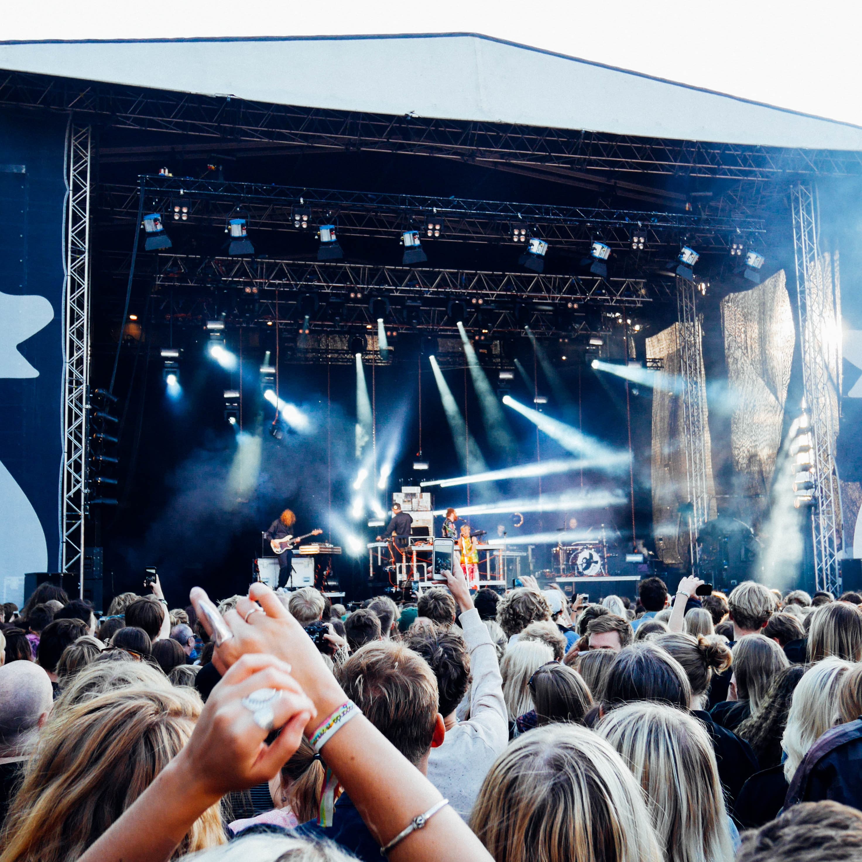 Large crowd watching a band perform on an outdoor stage with bright stage lights and smoke effects.