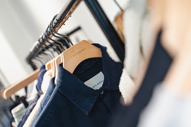 A dark blue shirt hangs on a wooden hanger branded "A DAY'S MARCH" in a well-lit store setting.