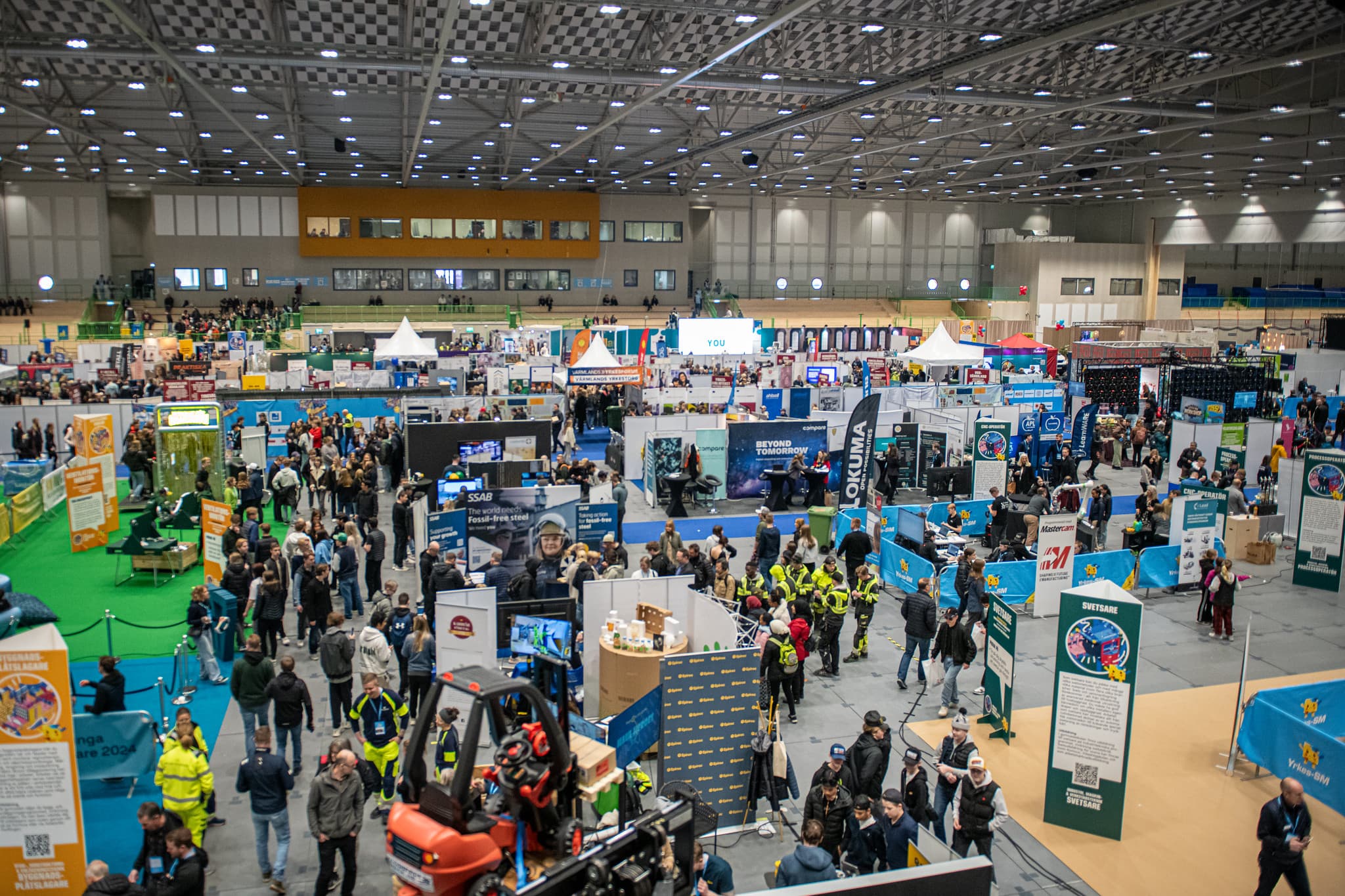 A large indoor exhibition hall filled with booths and crowds of people.