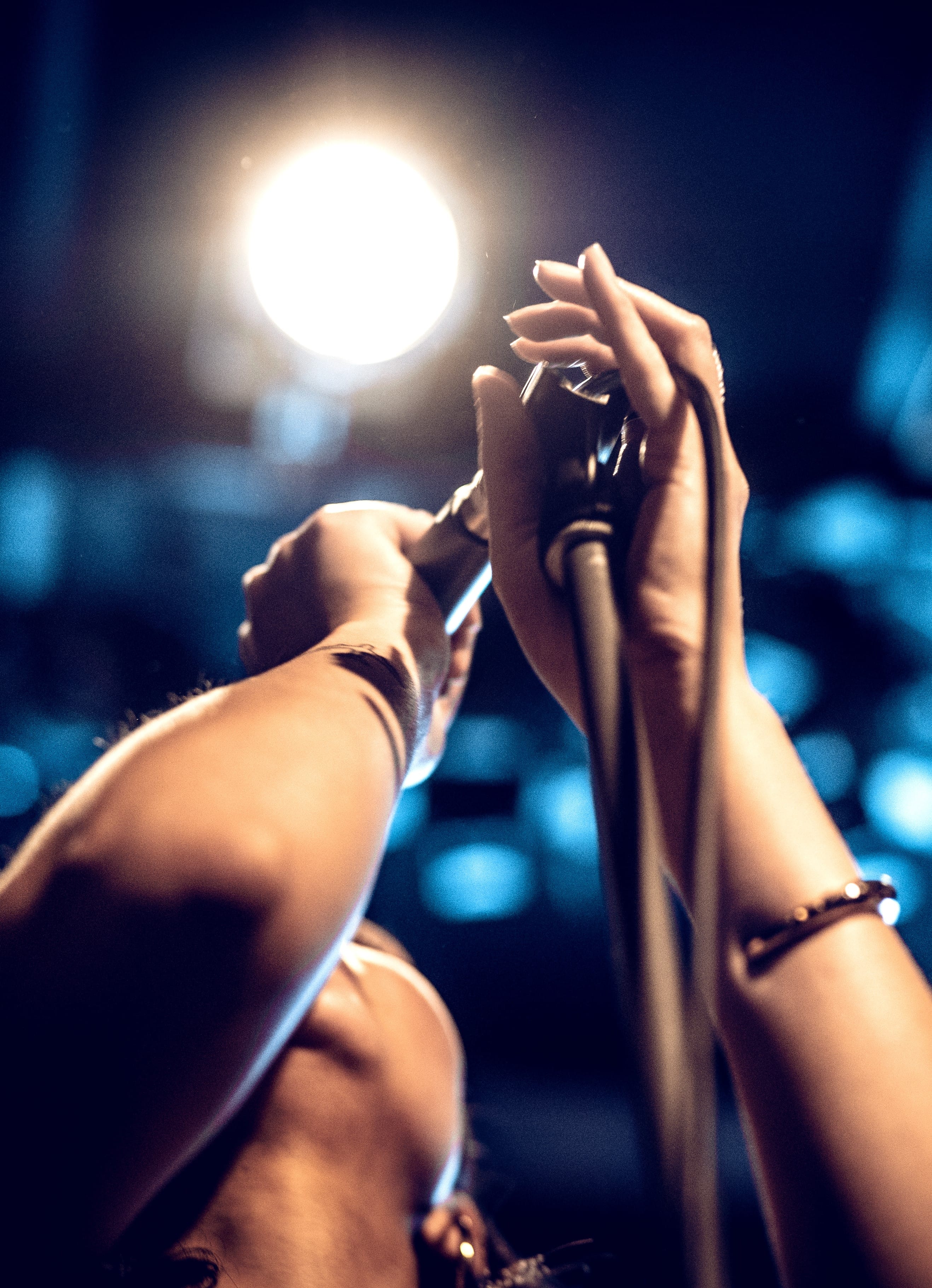 Hands holding a microphone under bright stage light, with dark background and blue highlights.