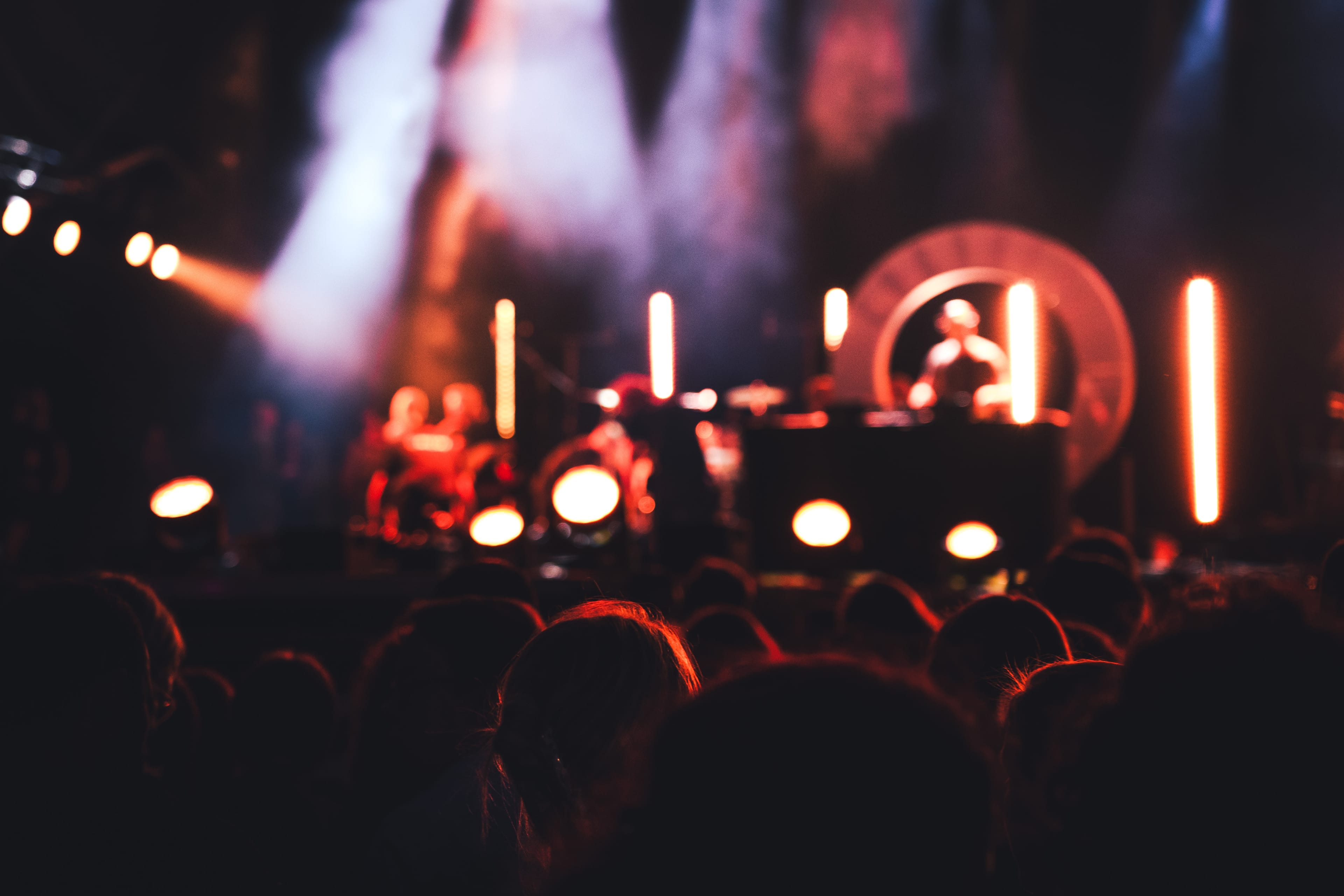 Dark silhouettes of a crowd in front of a stage with bright colored lights and a DJ performing.