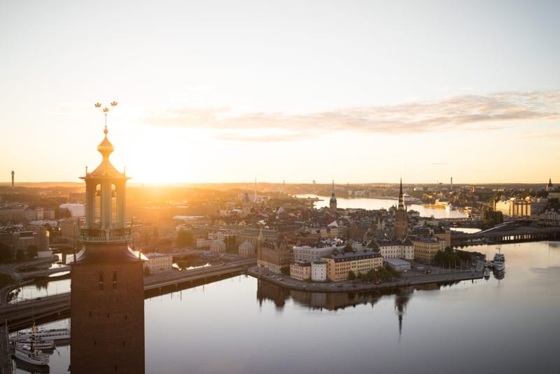 Aerial view of Stockholm City Hall tower backlit by the sun, with the Old Town and surrounding water glowing in soft morning light.