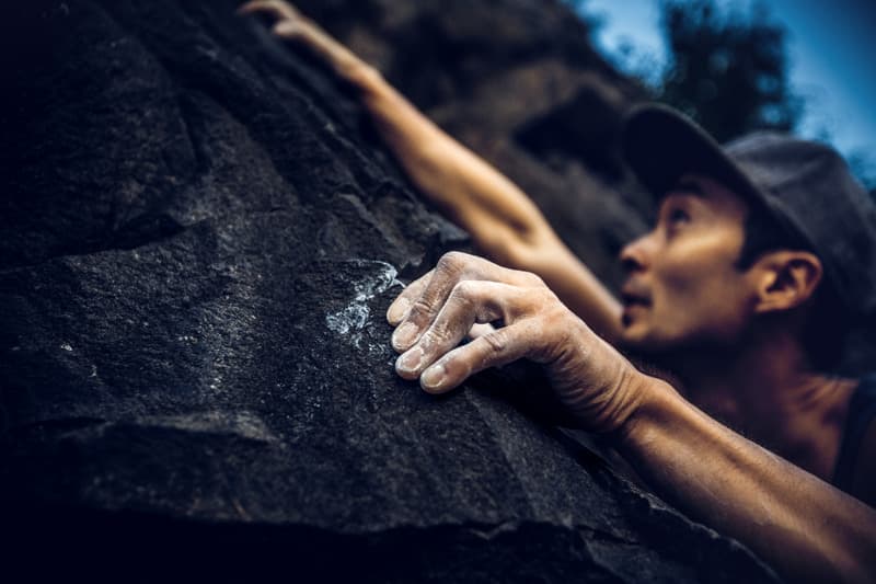 Close-up of a climber’s chalked hand gripping a rough rock face, with their face slightly out of focus in the background.