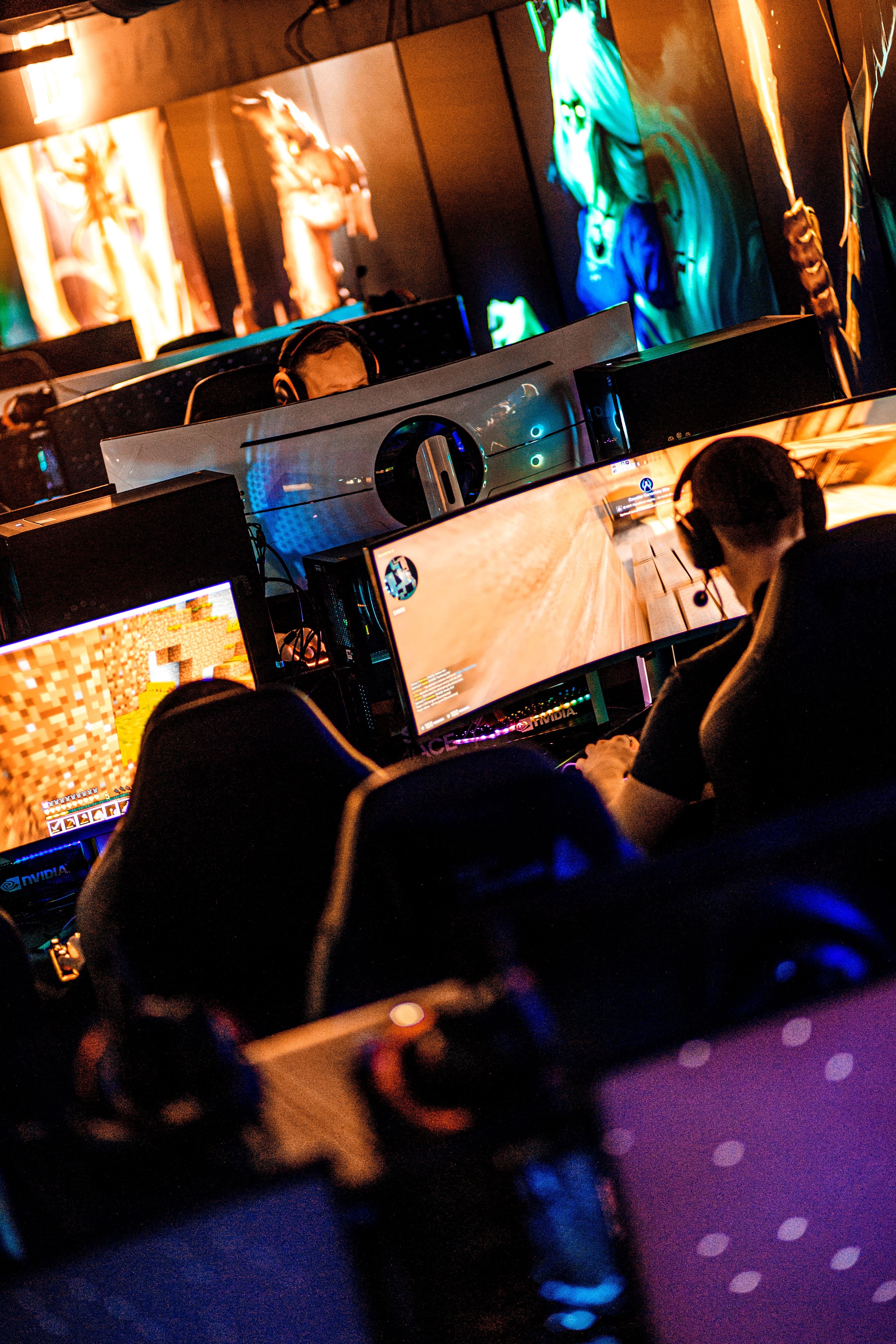 Several gamers wearing headsets sit at large monitors in a colorful esports gaming room.