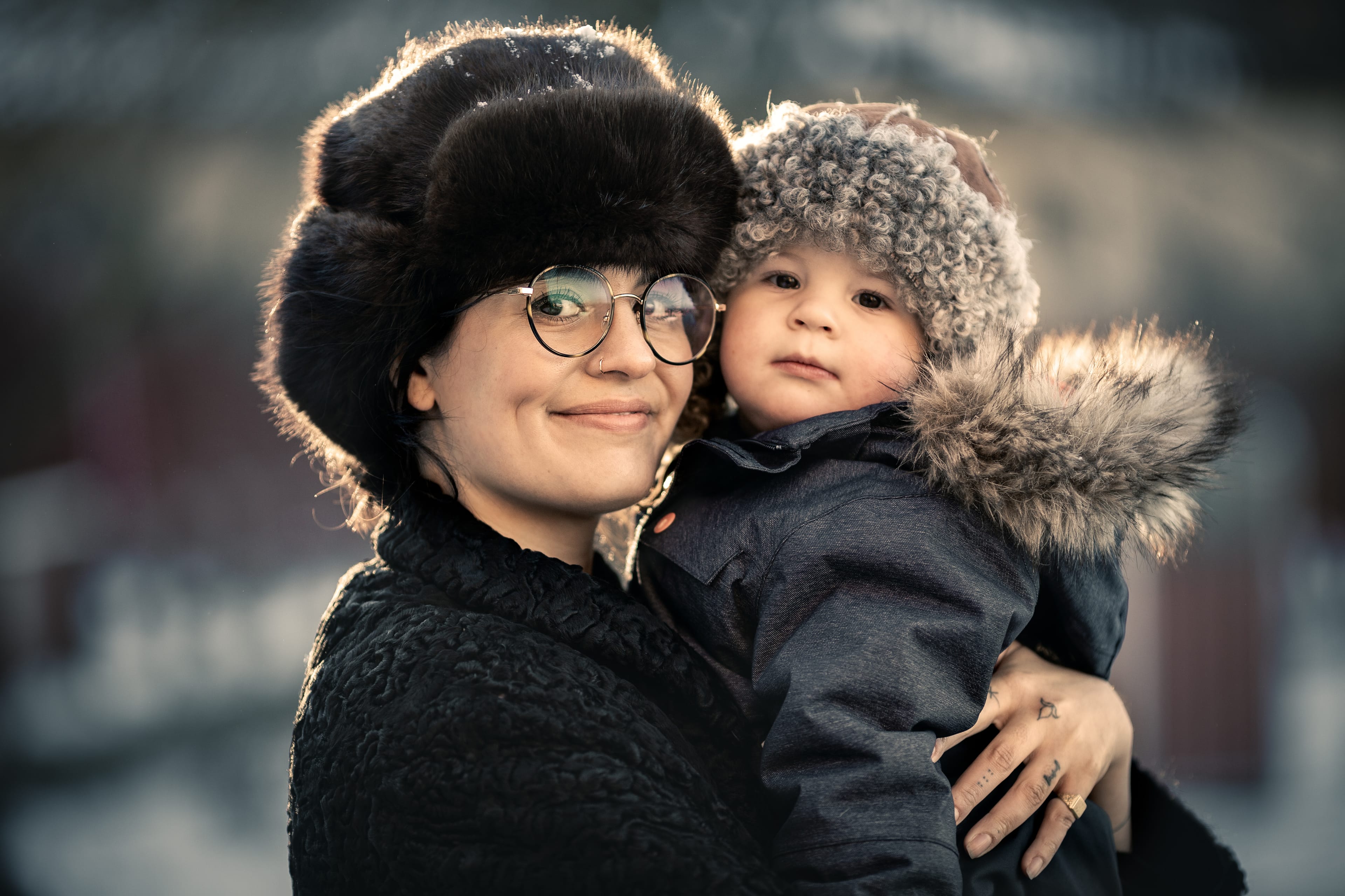 Close-up of a smiling adult and a child in cozy winter clothes and hats, snuggled together outdoors.
