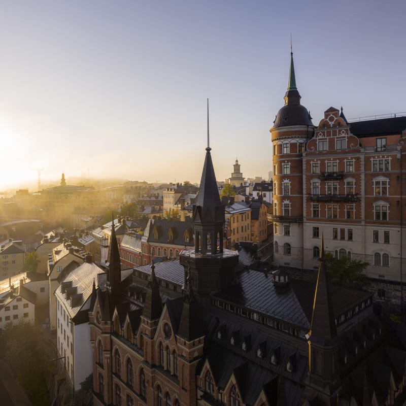 Aerial view of historic buildings and spires in Södermalm, Stockholm, bathed in soft morning light with a hint of mist on the horizon.