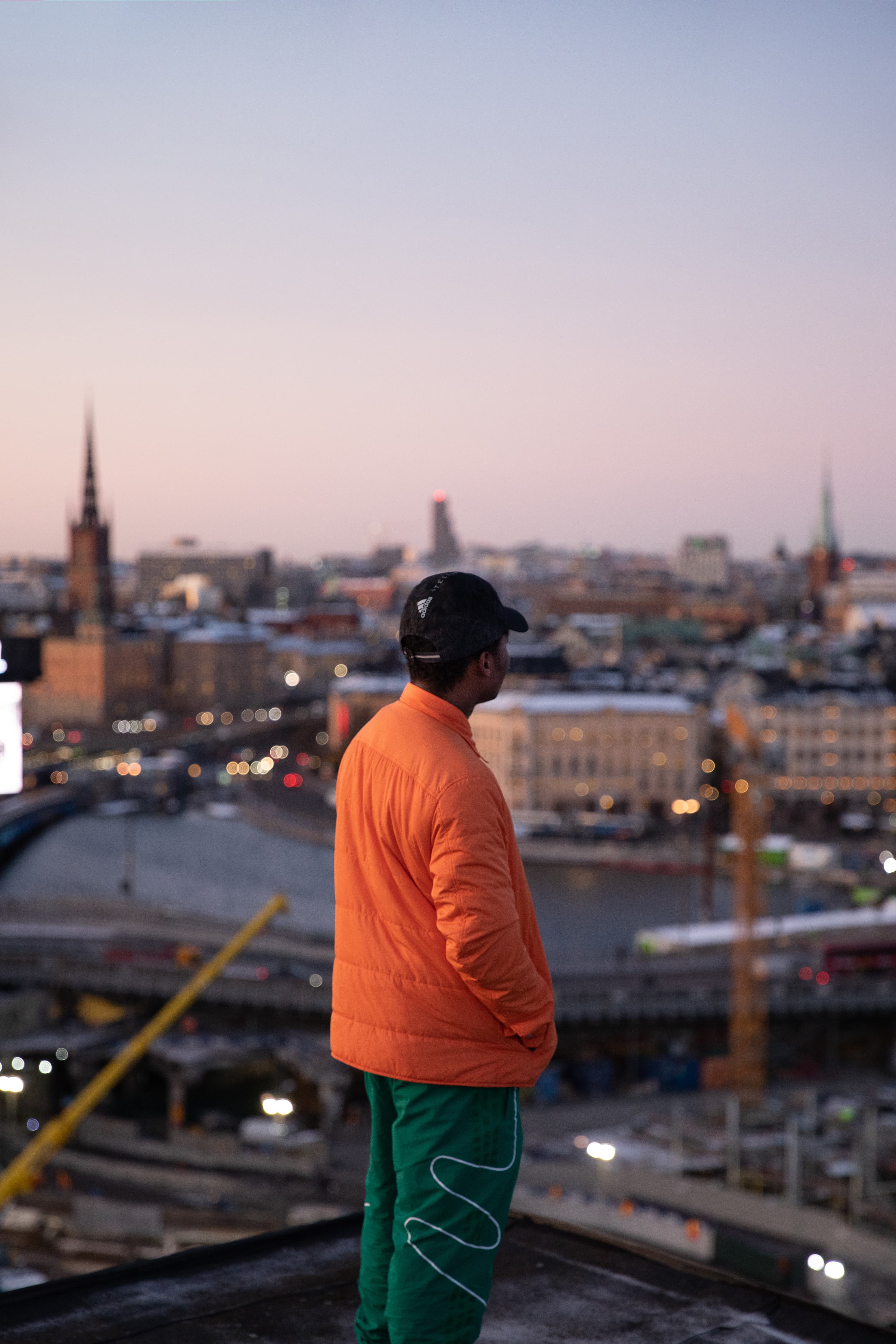 City view at dusk Person in an orange jacket standing on a rooftop, looking out over Stockholm’s skyline in the evening light.